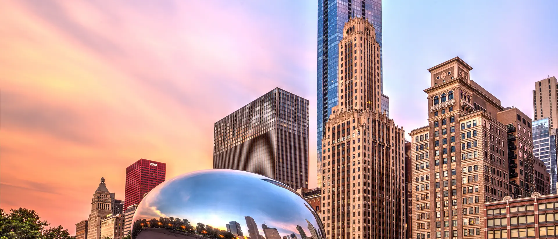 Cloud Gate sculpture reflects the skyline at sunset, surrounded by urban buildings in a vibrant city landscape.