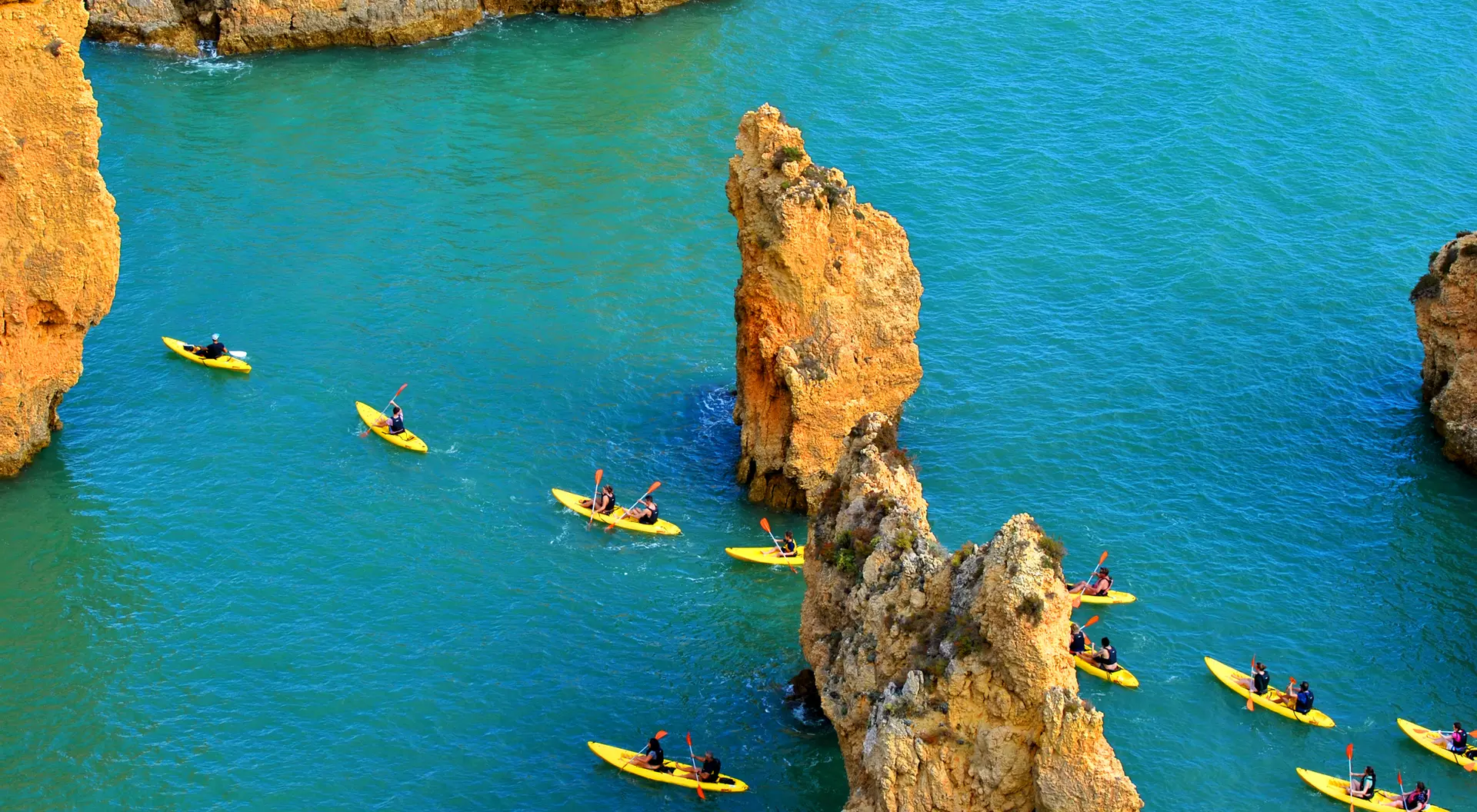 Aerial view of yellow kayaks paddling through turquoise water among rocky formations.
