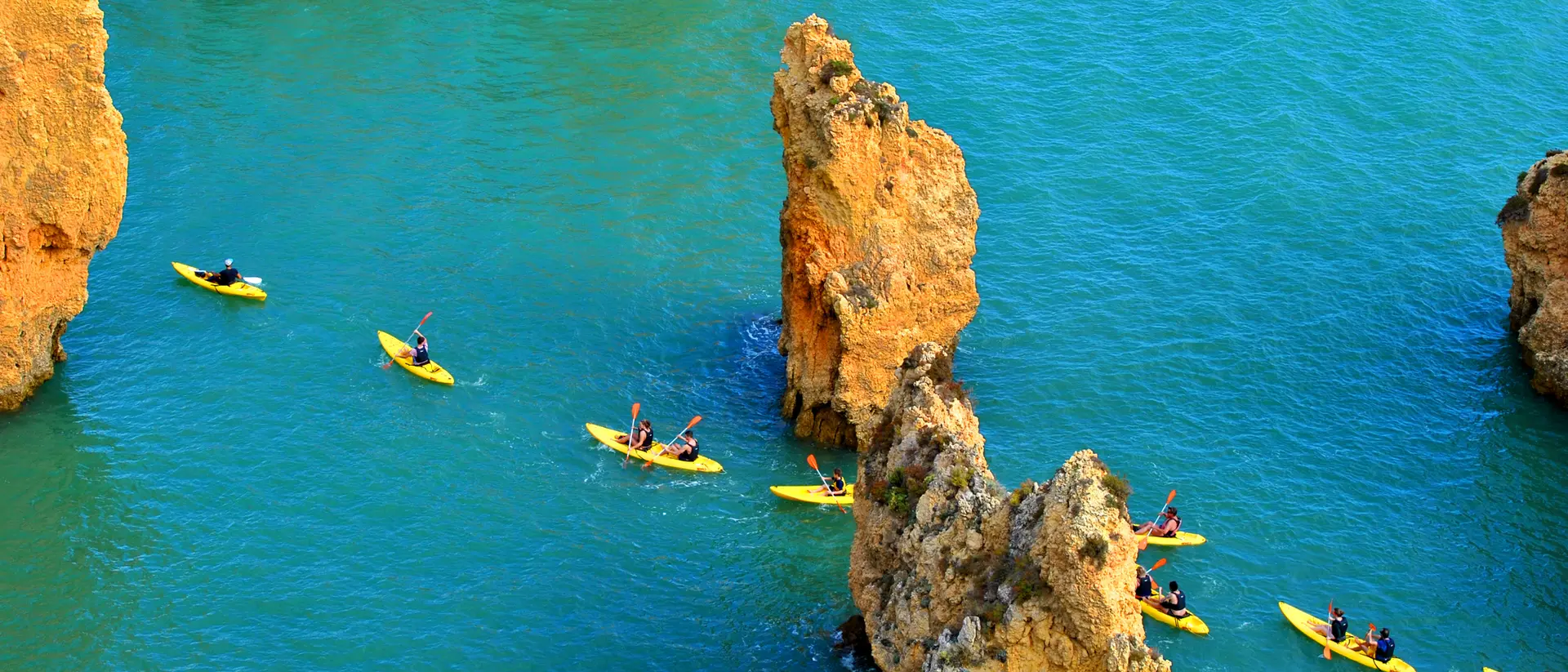 Aerial view of yellow kayaks paddling through turquoise water among rocky formations.