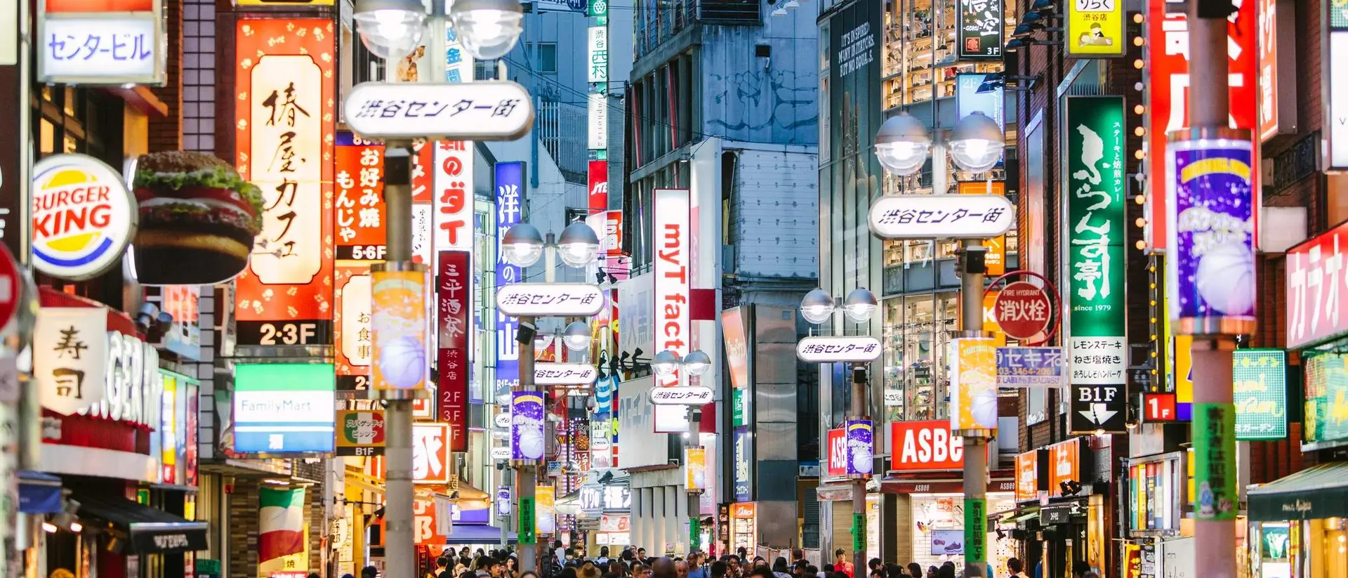 Busy street scene in a city, illuminated by colorful signs and bustling with people.