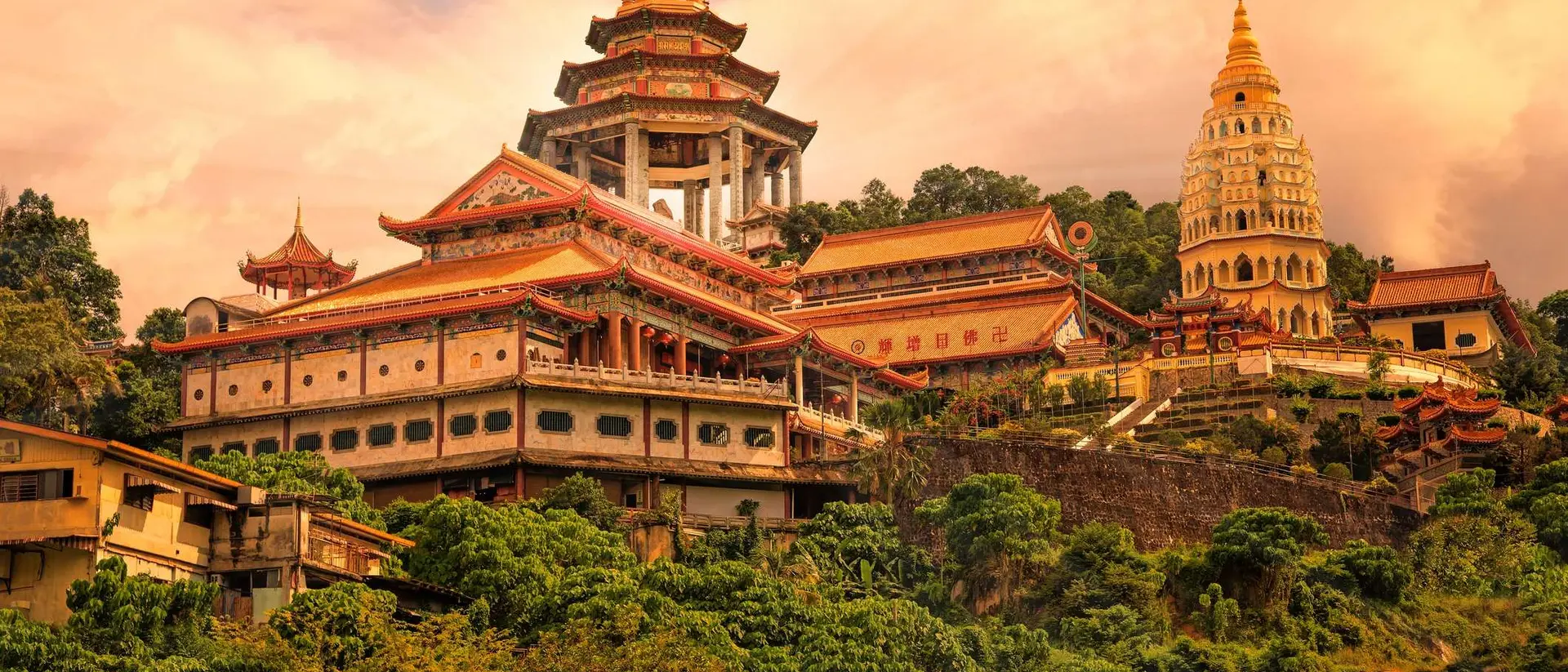 A scenic view of a majestic temple complex surrounded by lush greenery, with hills and a cloudy sky in the background.