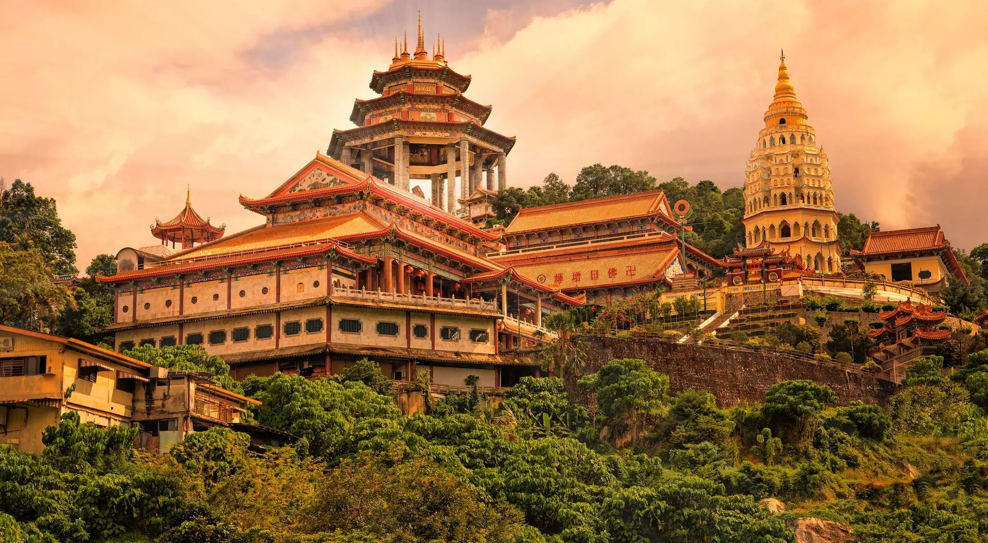 A scenic view of a majestic temple complex surrounded by lush greenery, with hills and a cloudy sky in the background.