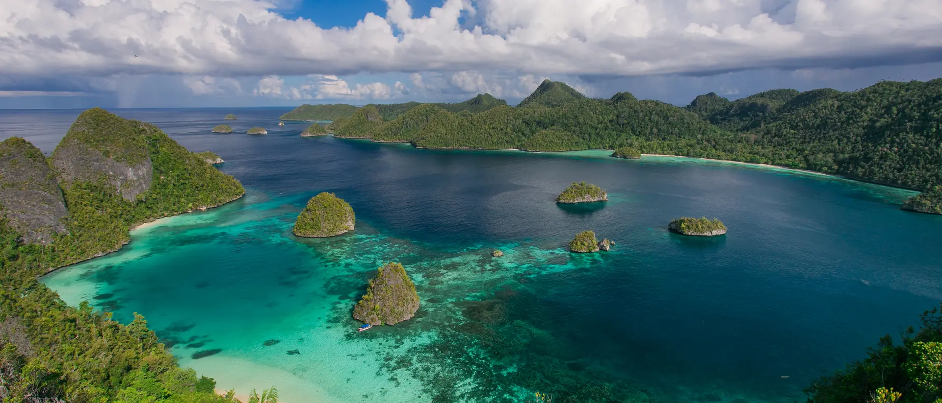 Aerial view of lush green islands surrounded by clear turquoise water and a blue sky with fluffy white clouds.
