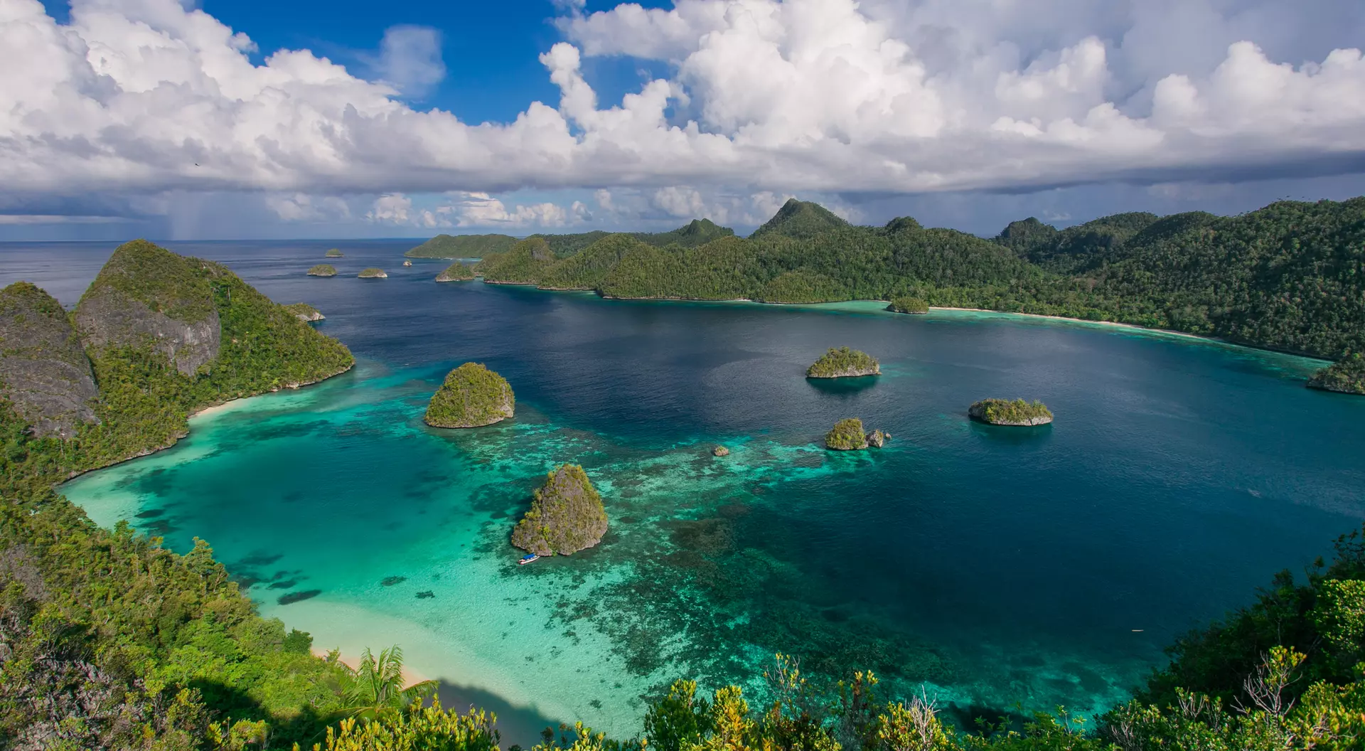 Aerial view of lush green islands surrounded by clear turquoise water and a blue sky with fluffy white clouds.