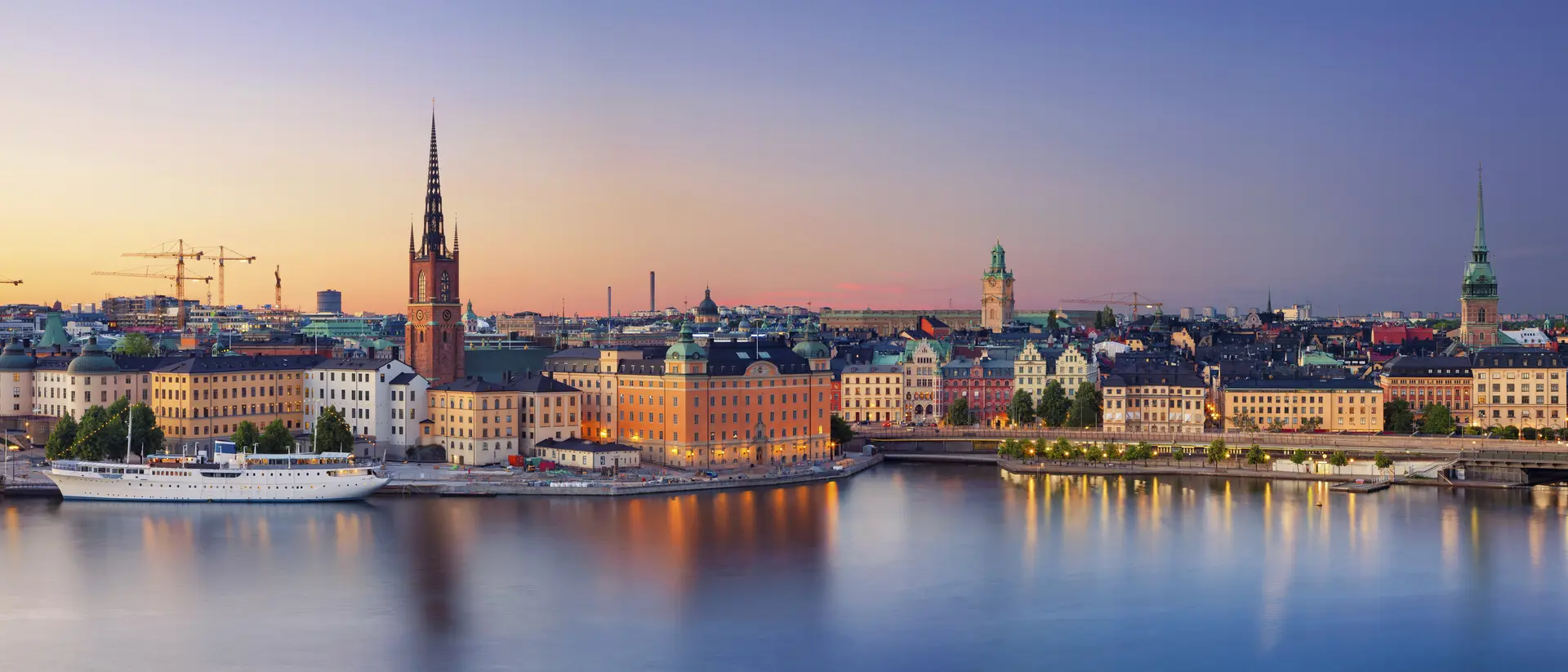 Panoramic view of Stockholm's waterfront at sunset, showcasing historic buildings and calm waters.