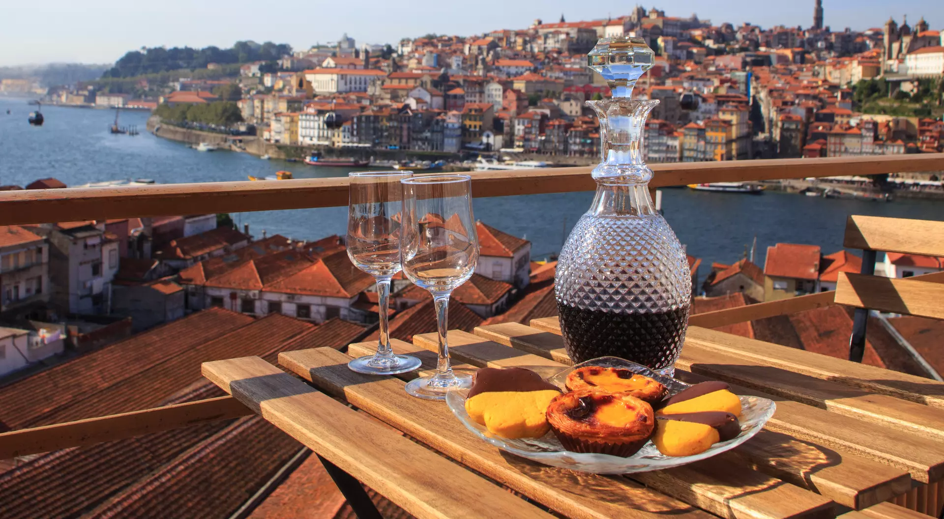 A beautiful view of a river and cityscape with a table set for wine and dessert, showcasing a relaxing outdoor scene.