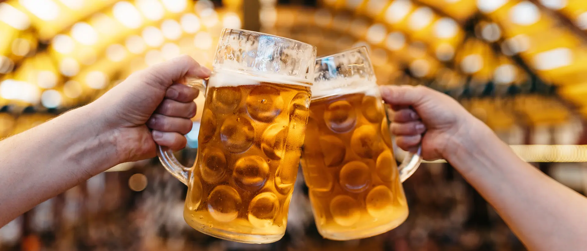 Two hands clinking beer glasses in octoberfest marquee.