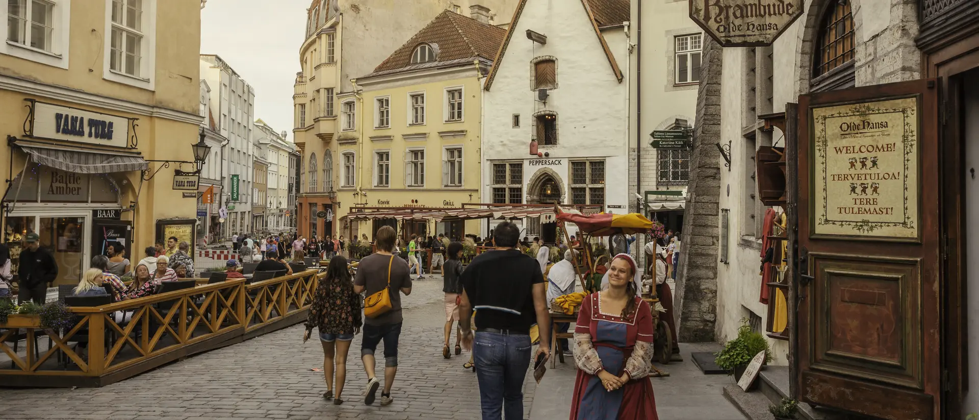A busy cobblestone street in a historic town, featuring shops, people walking, and a woman in traditional attire.