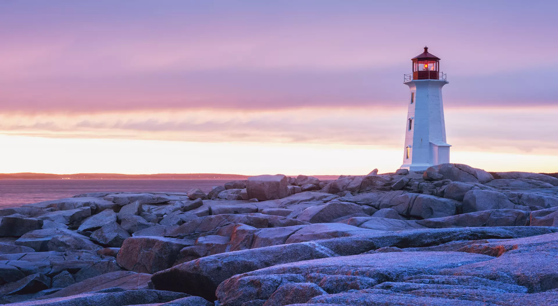 Nova Scotia The granite landscape surrounding Peggy's Cove Lighthouse is washed in sunset colours