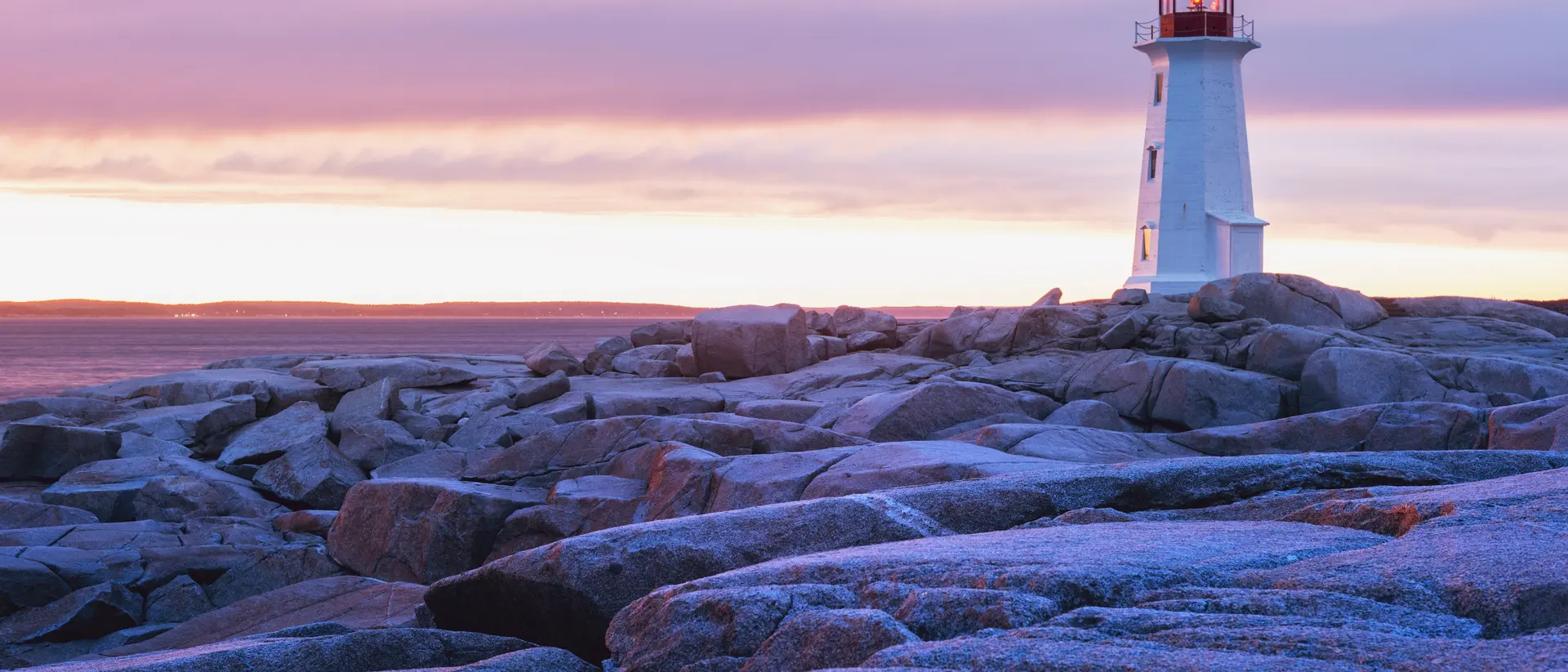 Nova Scotia The granite landscape surrounding Peggy's Cove Lighthouse is washed in sunset colours