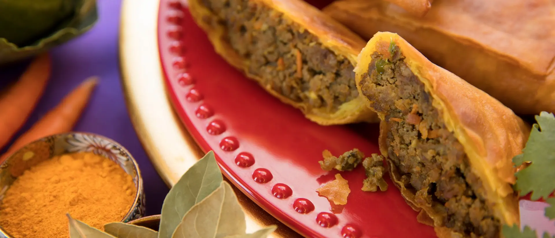 A plate of savory spring rolls filled with seasoned meat, surrounded by spices and fresh vegetables.