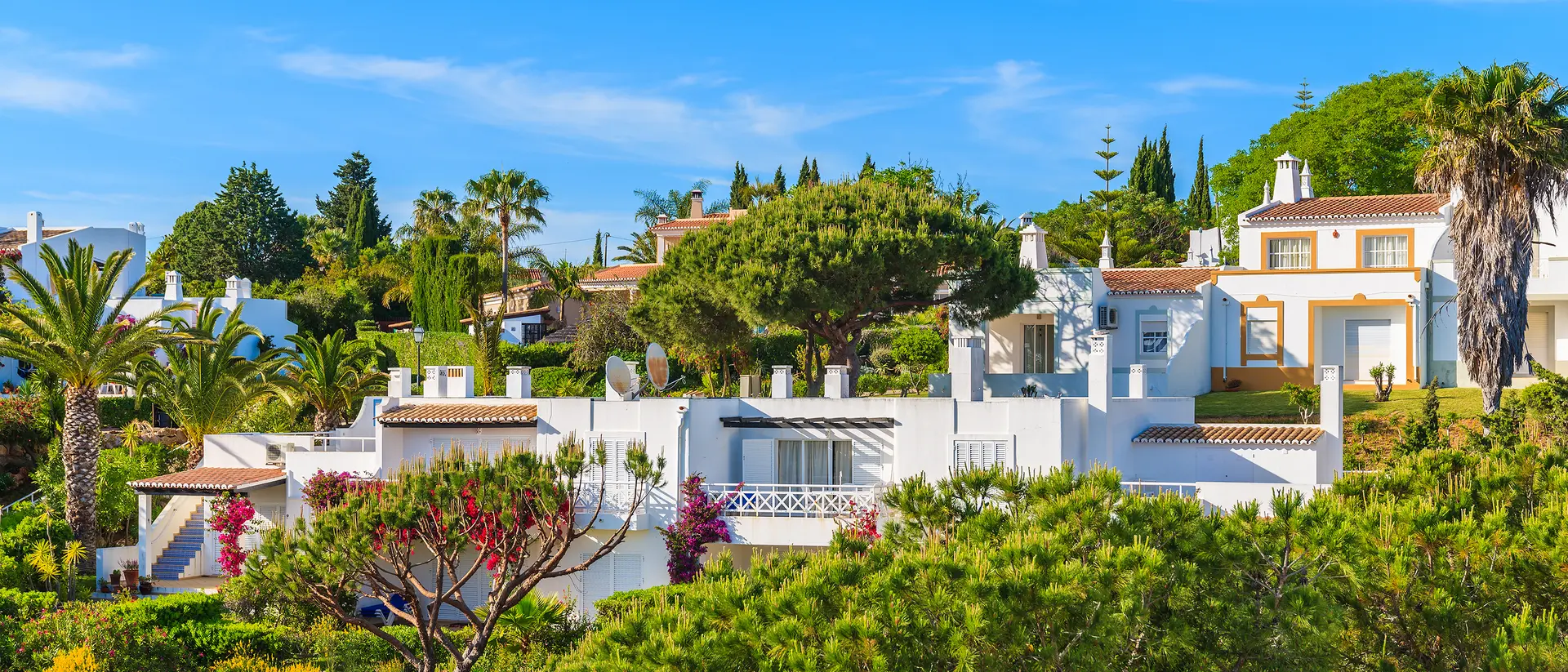 White villas surrounded by lush greenery and palm trees under a clear blue sky.