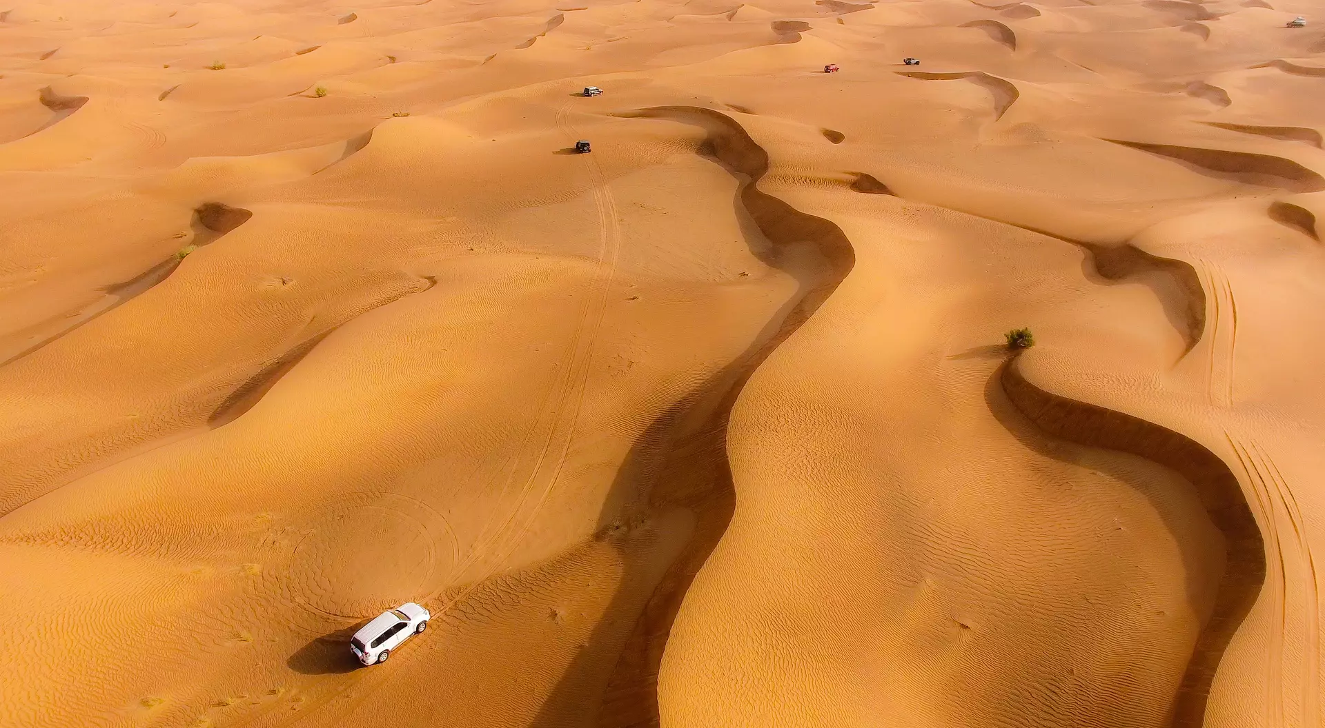 Aerial view of rolling sand dunes with a vehicle navigating through the desert landscape.