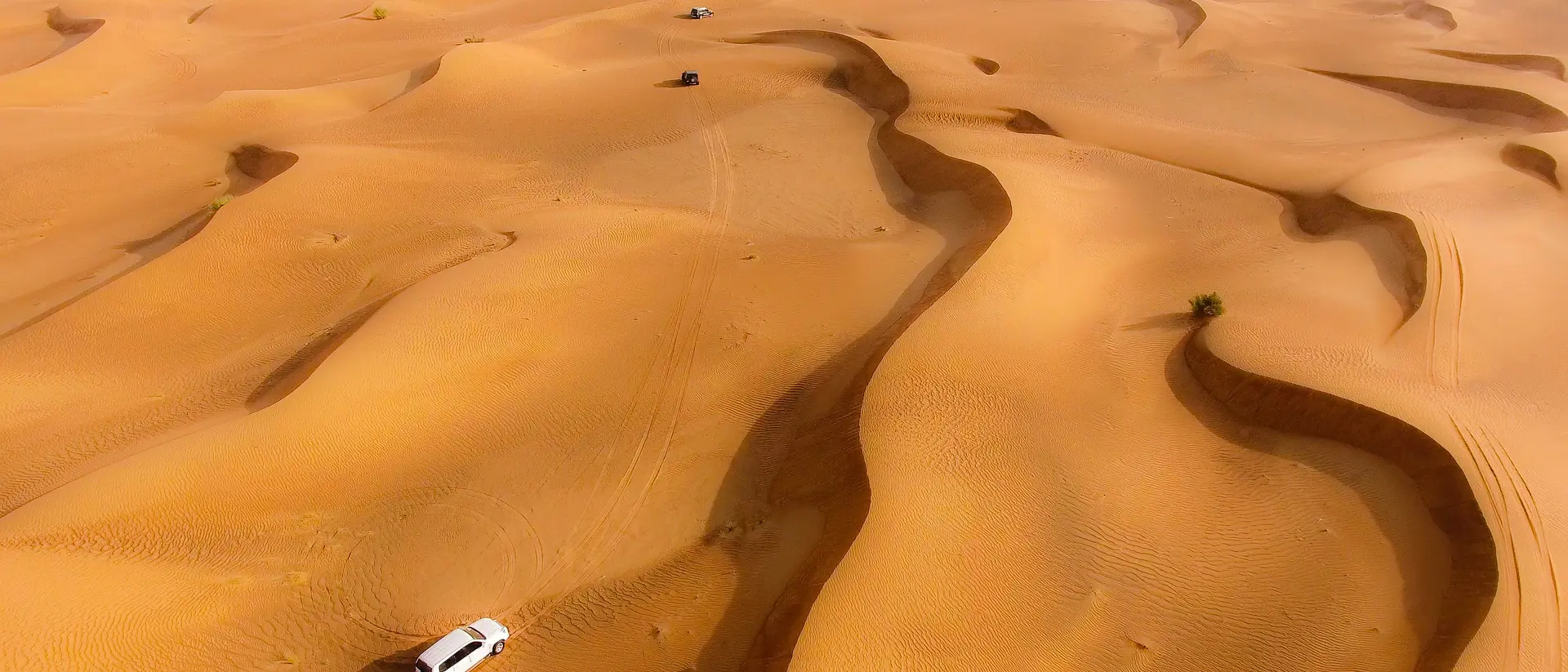Aerial view of rolling sand dunes with a vehicle navigating through the desert landscape.