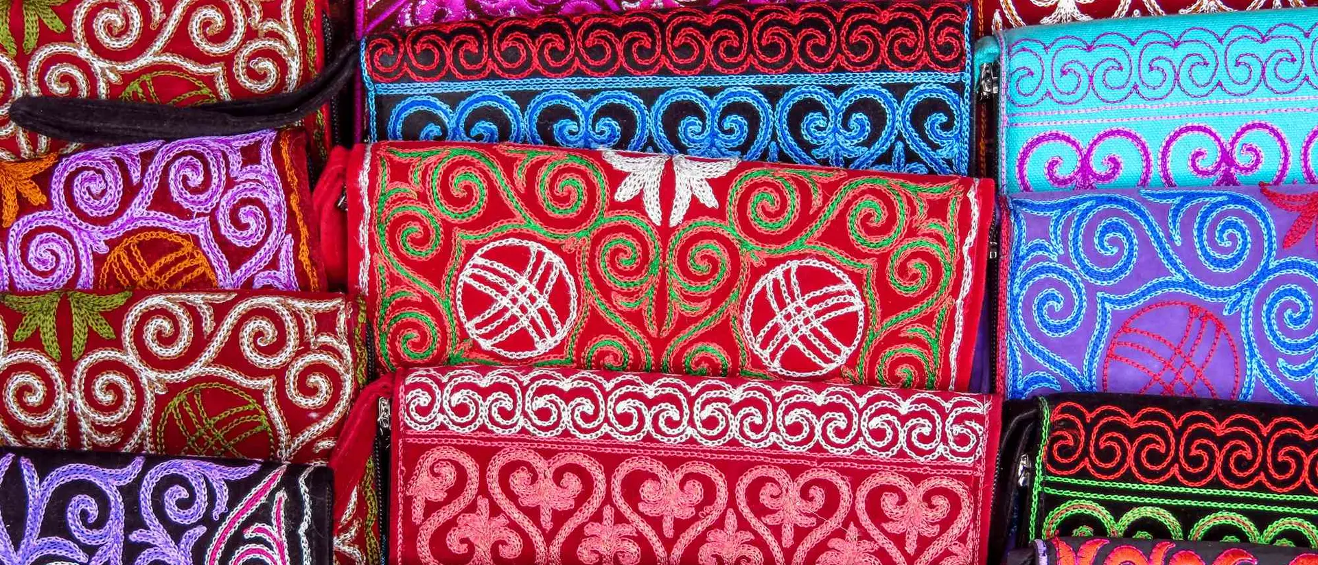 Colorful fabric pouches with intricate embroidery patterns in various shades of red, pink, blue, and black.
