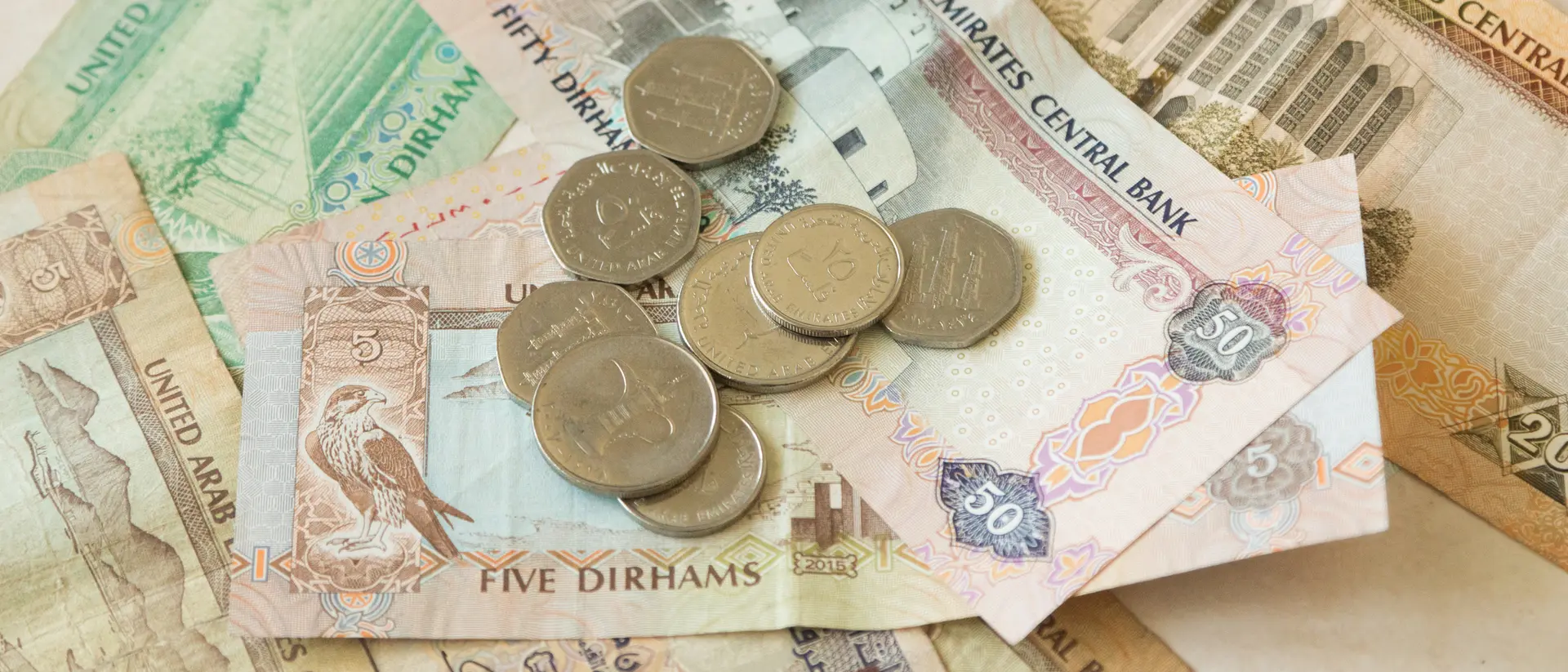 A pile of United Arab Emirates dirham banknotes and coins, featuring various denominations and designs.
