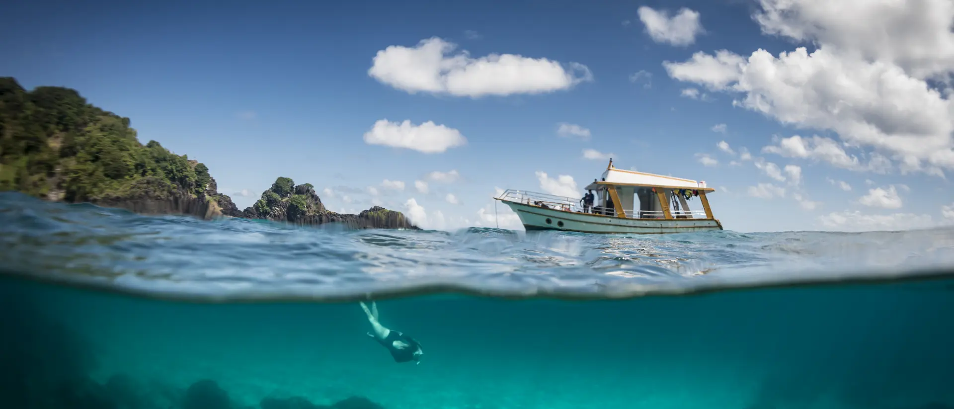 View of a tour boat and a woman free diving at 'Sancho' beach in the archipelago of Fernando de Noronha