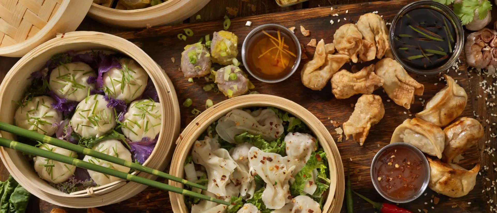A spread of various Asian dumplings and spring rolls, served in bamboo steamers and accompanied by dipping sauces.