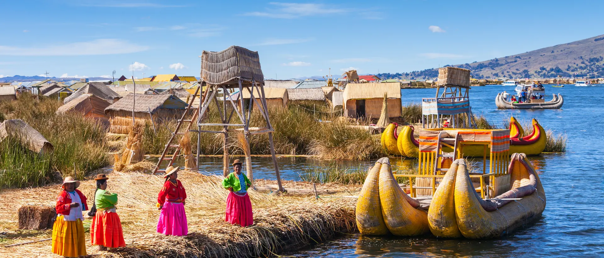 Colorful traditional boats and local women in vibrant clothing by the floating islands on a lake under a clear blue sky.
