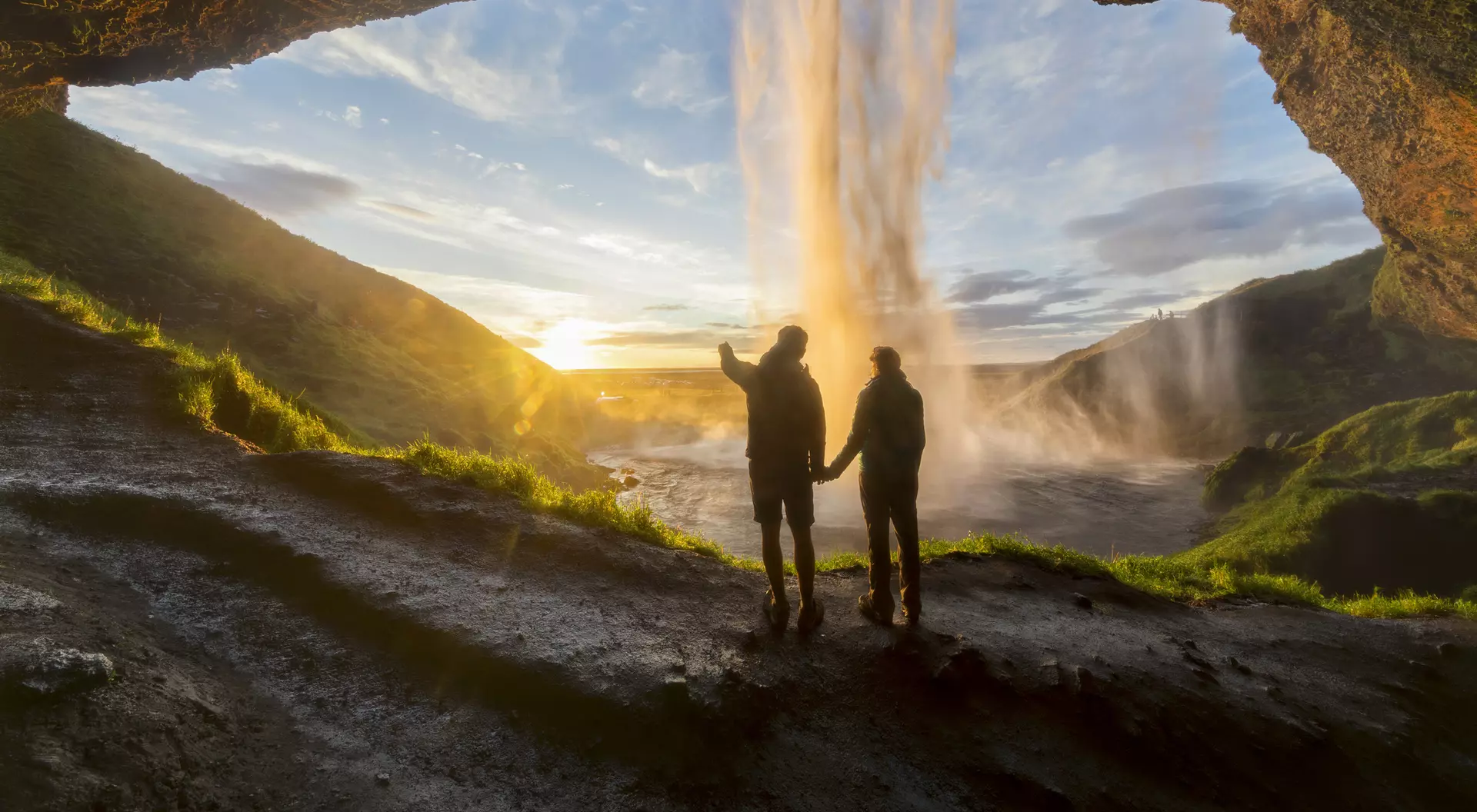 Discover the magic of Seljalandsfoss, Iceland, with those who matter most. Tourists under waterfall in Seljalandsfoss, Iceland, man pointing with finger to the sun