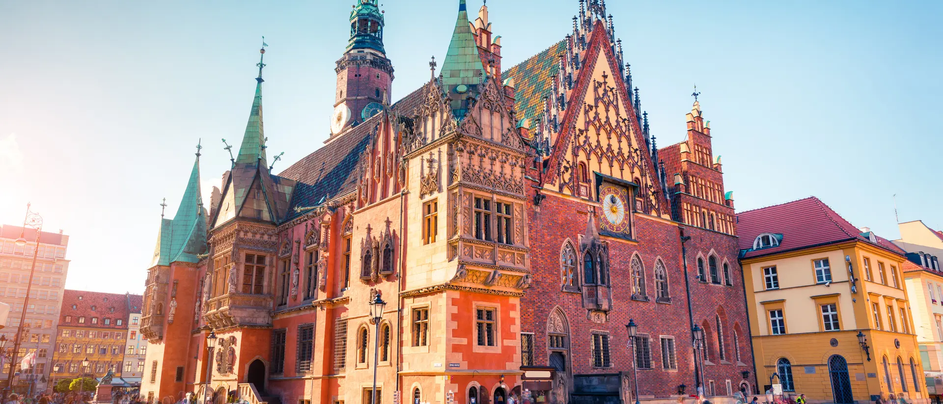 Historic building with intricate architectural details, set in a lively square filled with people and shops.