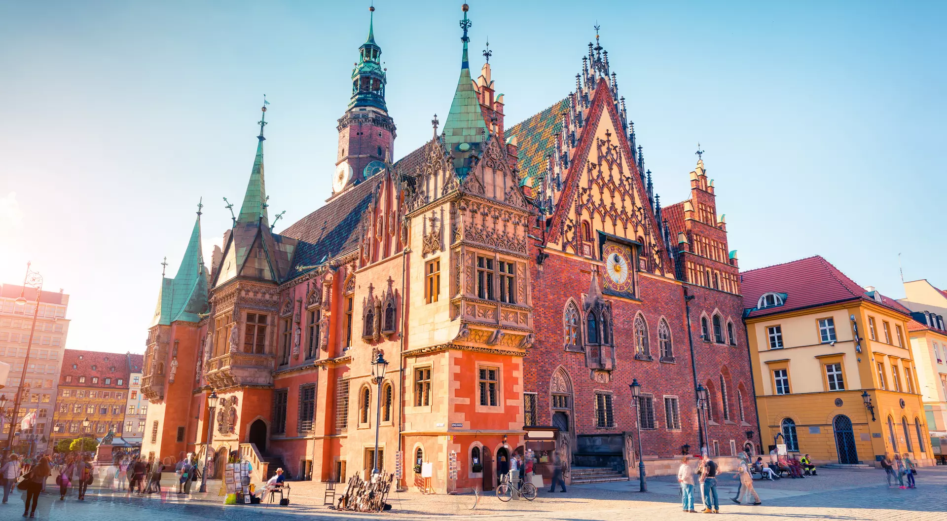 Historic building with intricate architectural details, set in a lively square filled with people and shops.
