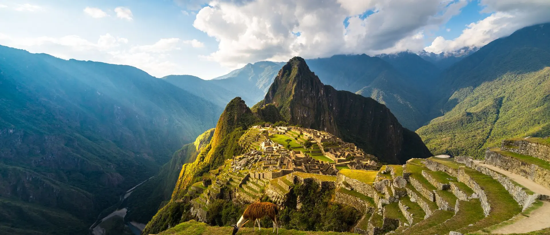 Machu Picchu illuminated by the warm sunset light. Wide angle view from the terraces above with scenic sky and sun burst