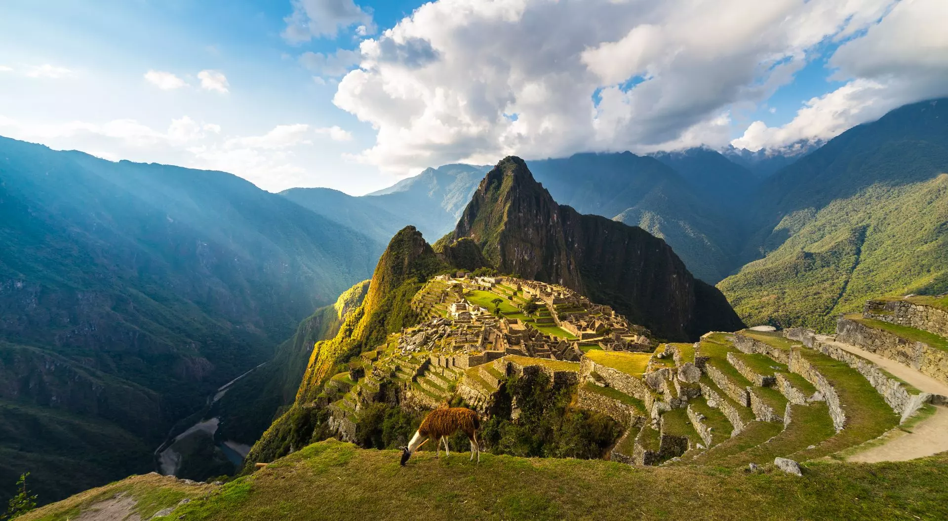 Machu Picchu illuminated by the warm sunset light. Wide angle view from the terraces above with scenic sky and sun burst