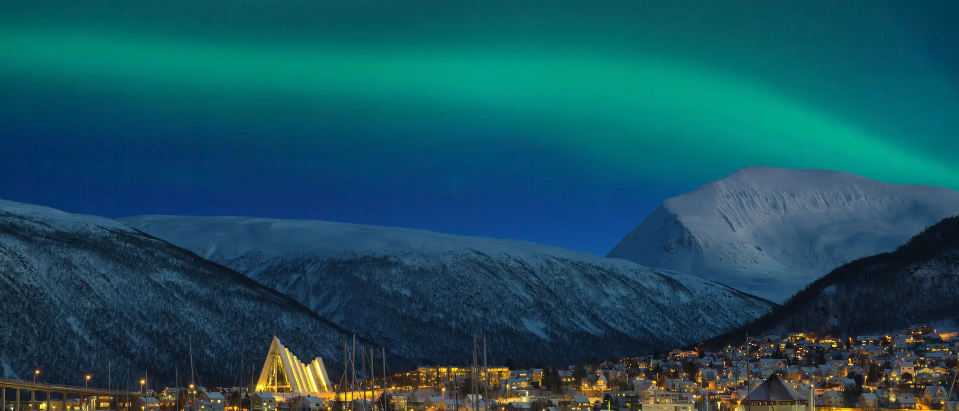 Aurora Borealis View at night on illuminated Tromso city with cathedral and majestic aurora borealis
