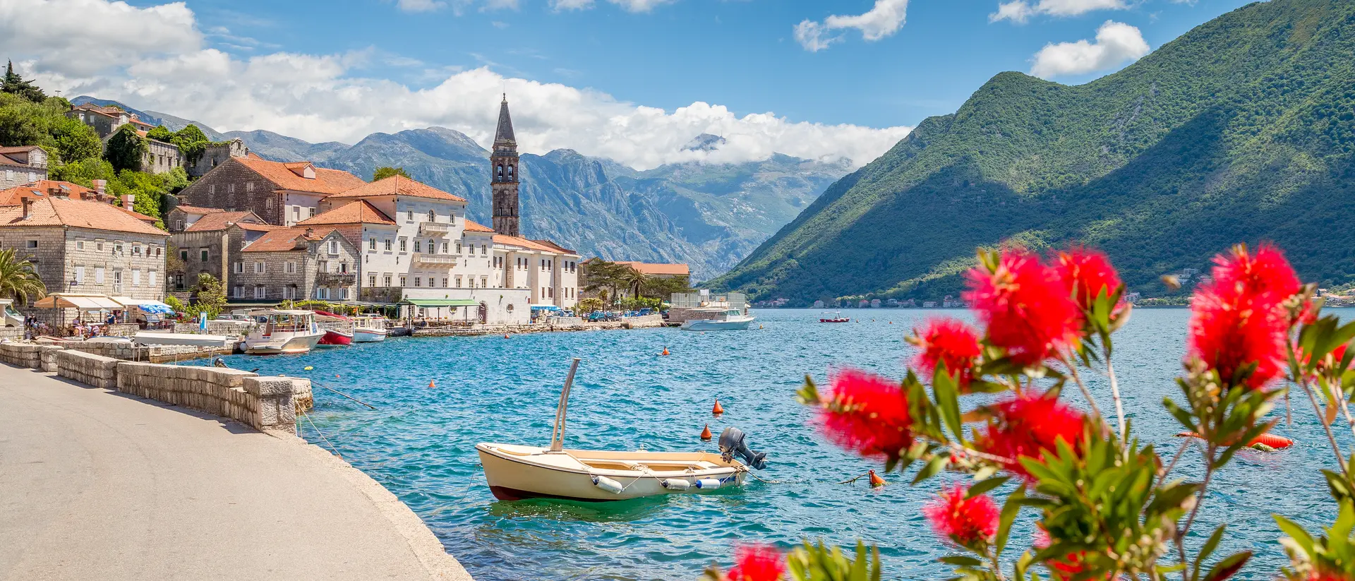 Panorama view of Perast at famous Bay of Kotor with blooming flowers on a beautiful sunny day with blue sky and clouds in summer