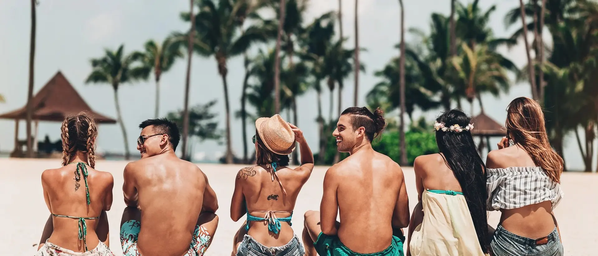 Seven people sitting on a beach, enjoying the sun, with palm trees in the background.