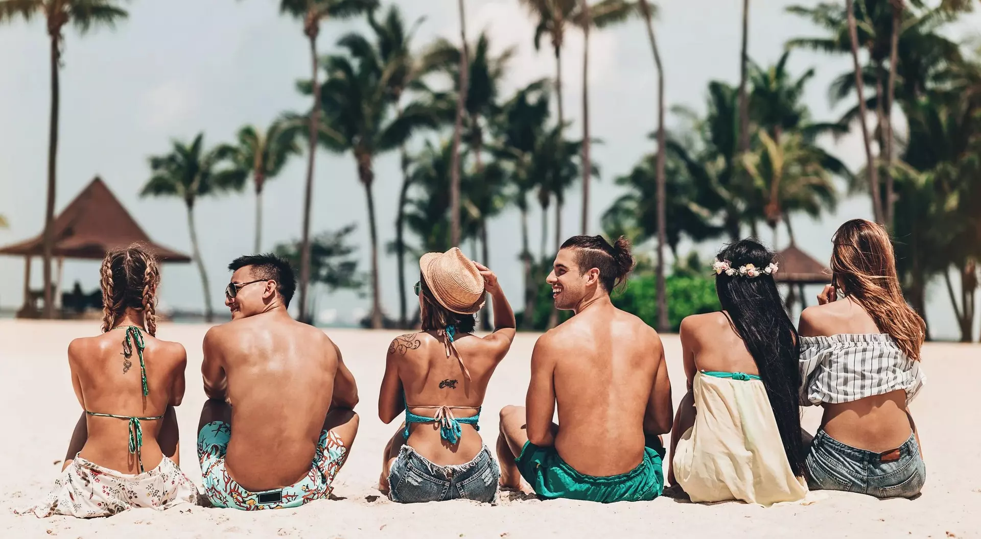 Seven people sitting on a beach, enjoying the sun, with palm trees in the background.
