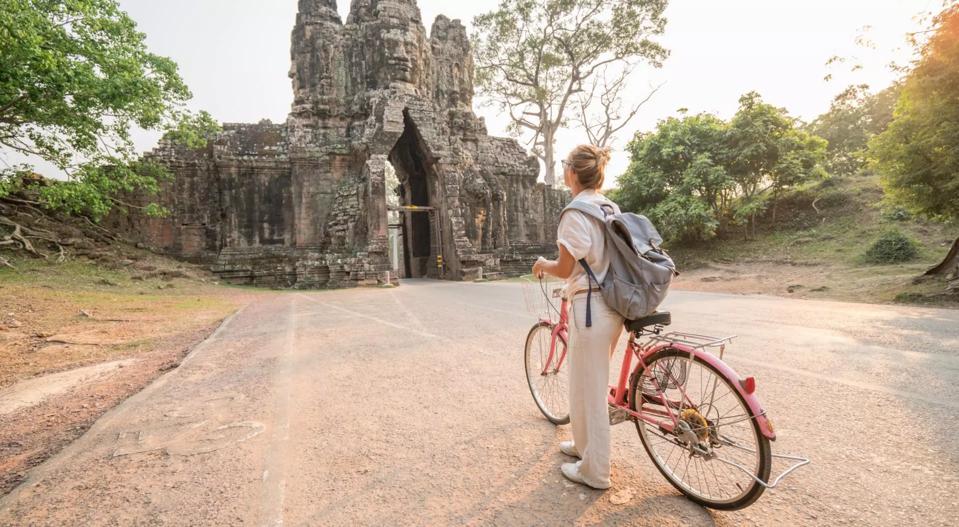 Young woman traveling in Cambodia visiting the temples of Angkor wat complex by bicycle.