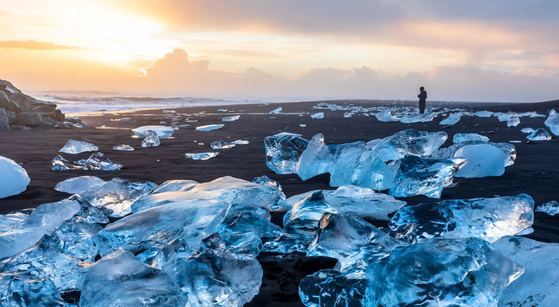 Diamond Beach in Iceland with blue icebergs melting on the black sand and ice glistening with sunrise sun light