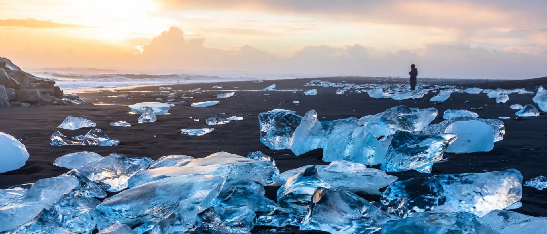 Diamond Beach in Iceland with blue icebergs melting on the black sand and ice glistening with sunrise sun light