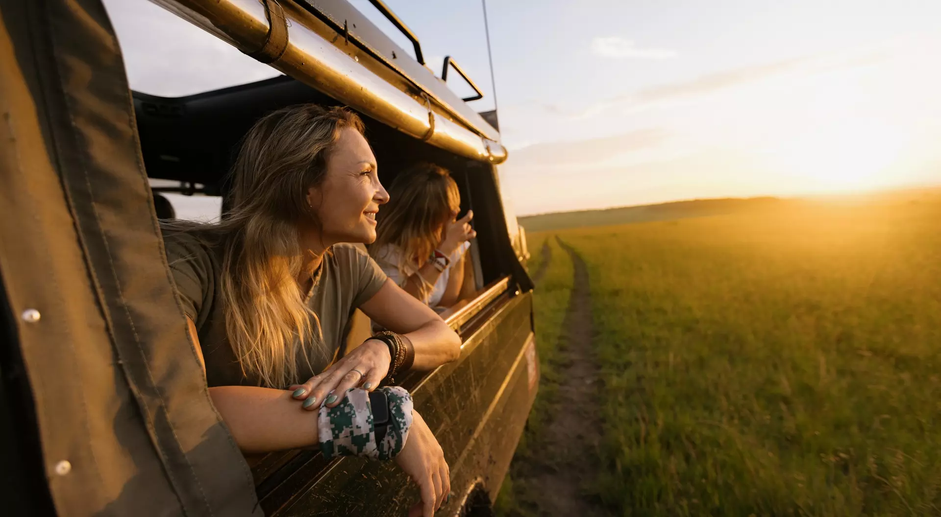 A woman in a Land Cruiser on a safari game drive at sunset leaning out of the vehicle window.
