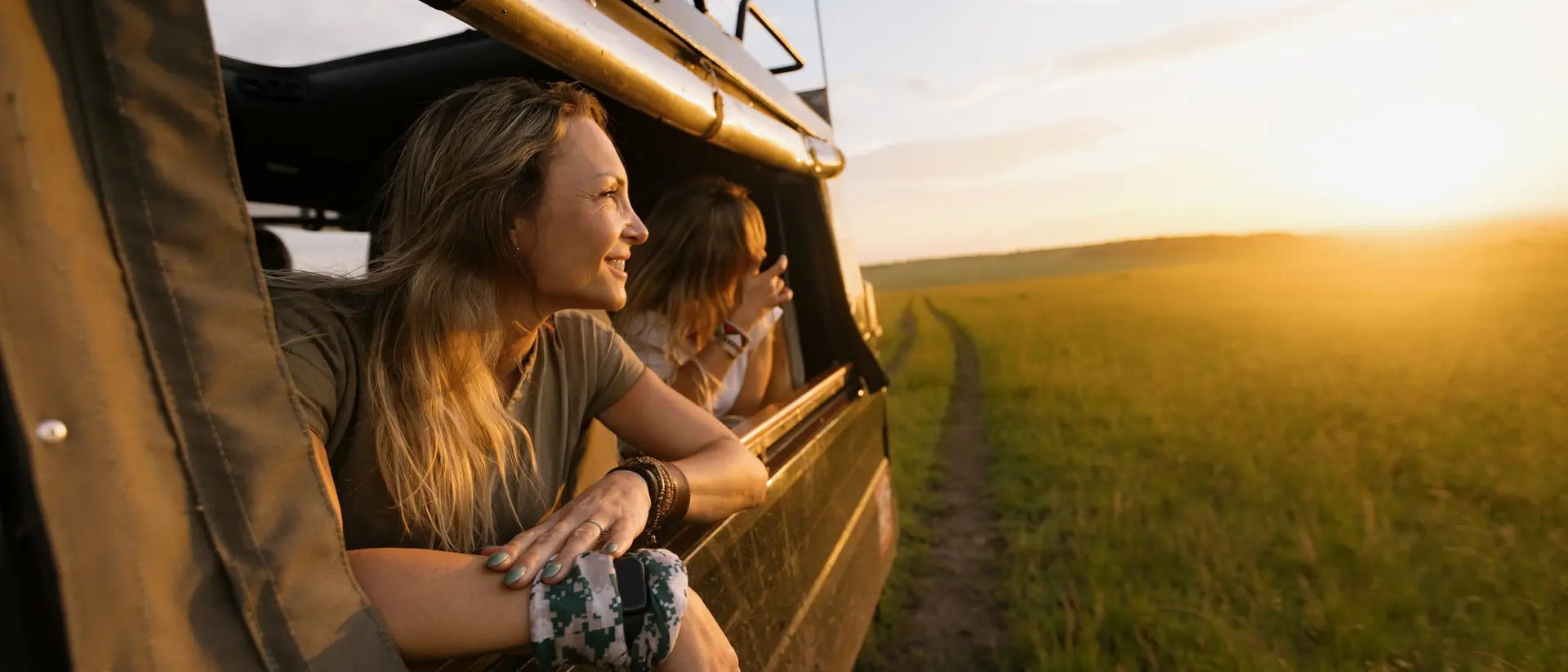 Kenya A woman in a Land Cruiser on a safari game drive at sunset leaning out of the vehicle window.
