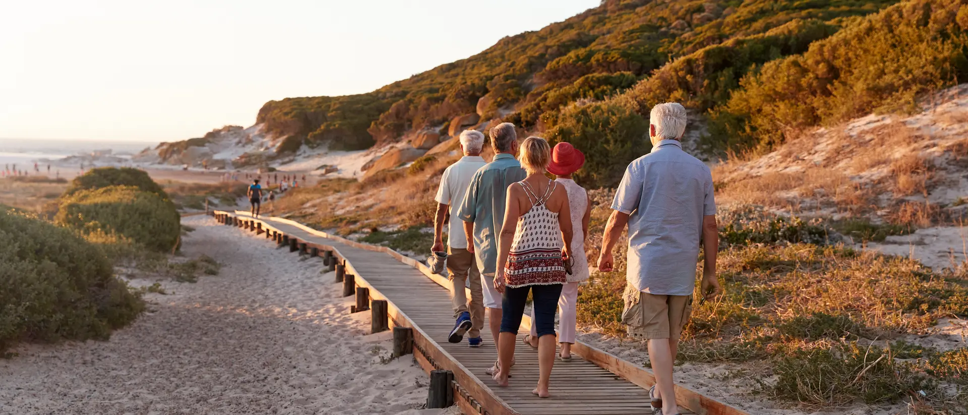 Group Of Senior Friends Walking Along Boardwalk At Beach On Summer Group Vacation