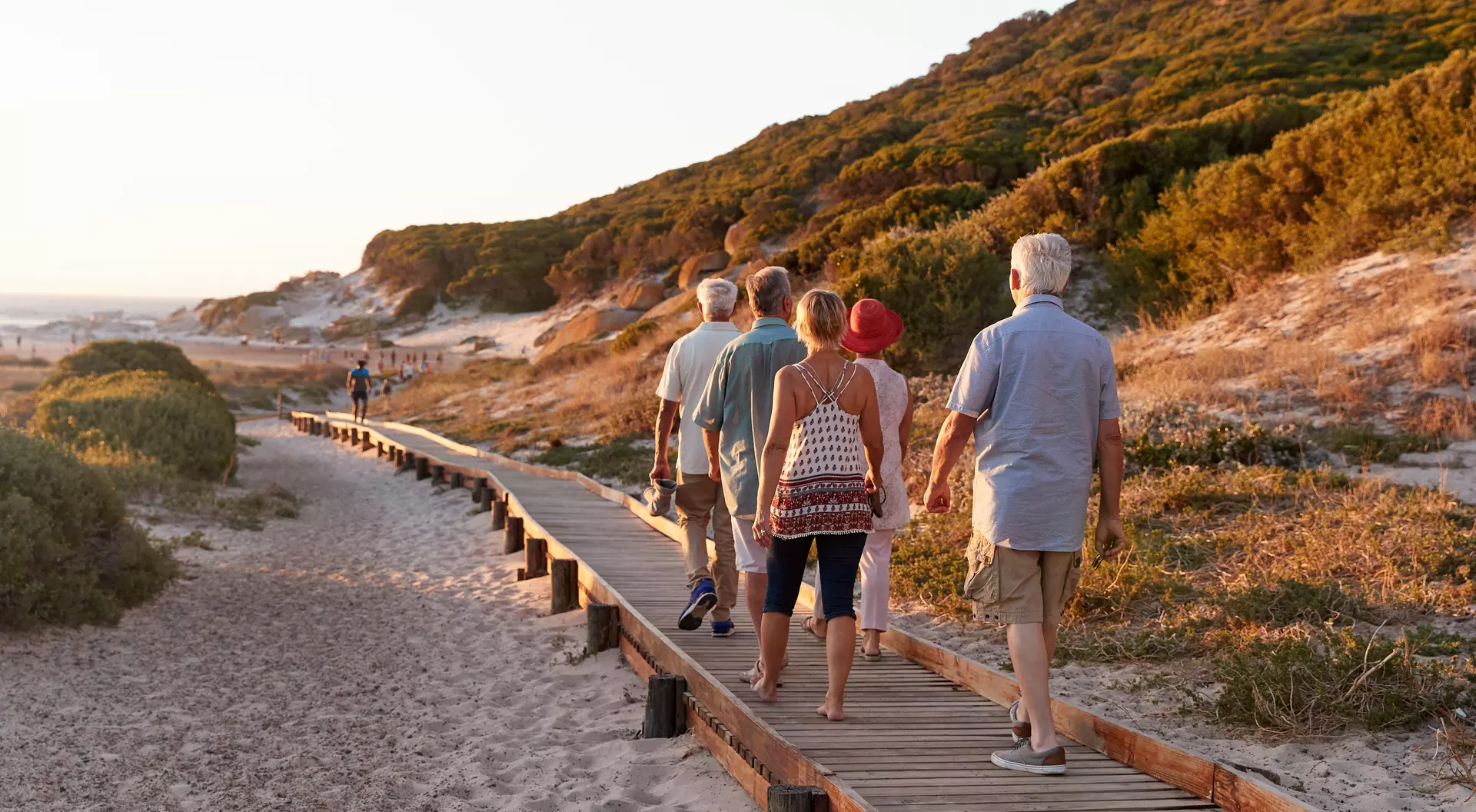 Group Of Senior Friends Walking Along Boardwalk At Beach On Summer Group Vacation