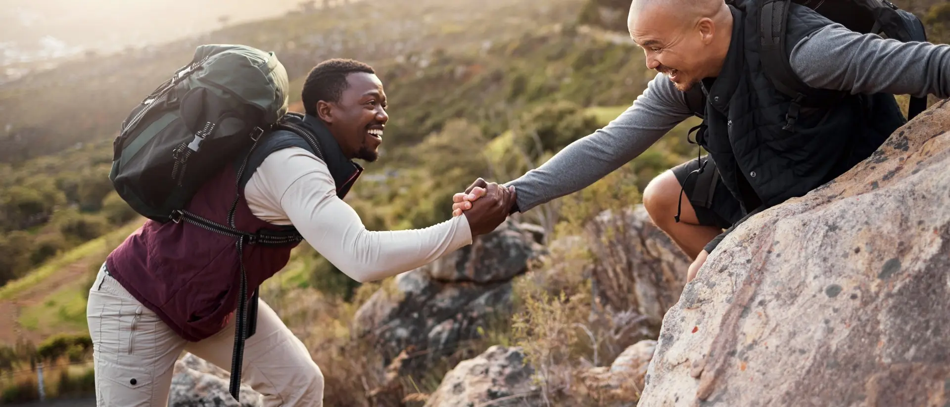 two hikers help each other get over rocks on a mountain