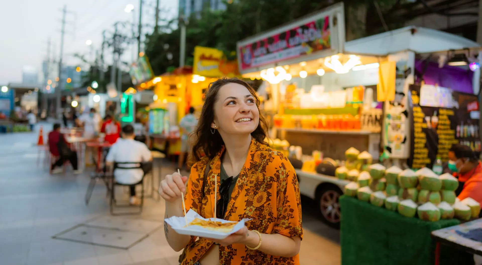 Cheerful woman eating thai pancakes (roti) on night market in Bangkok