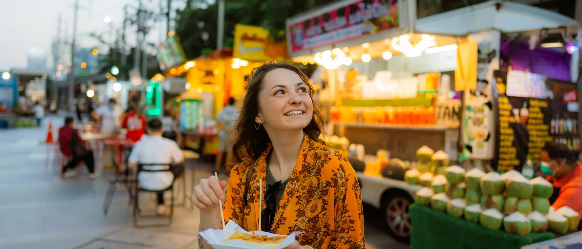 Cheerful woman eating thai pancakes (roti) on night market in Bangkok