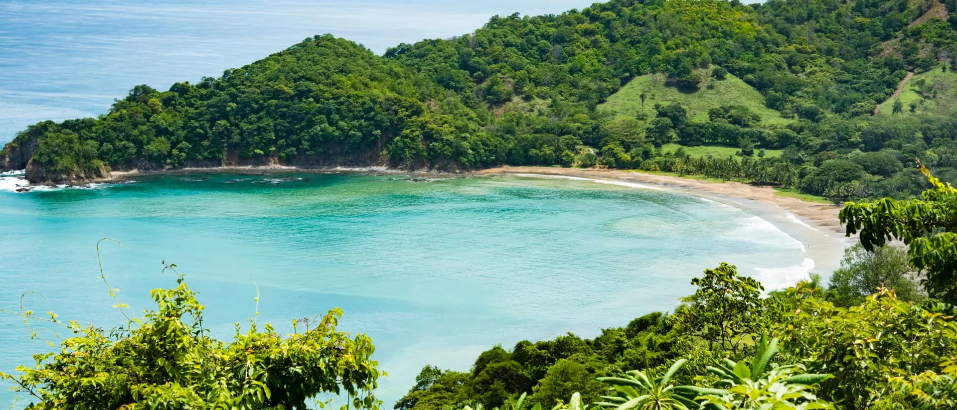 View of a small crescent beach hidden away among green hills and forests