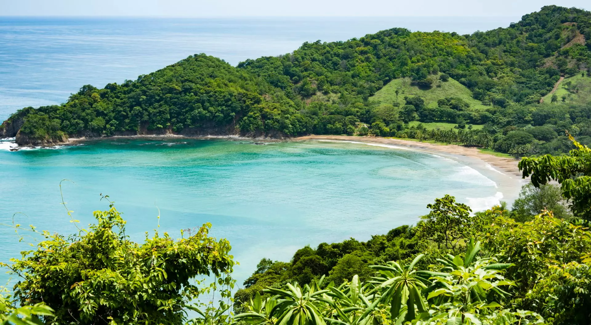 View of a small crescent beach hidden away among green hills and forests