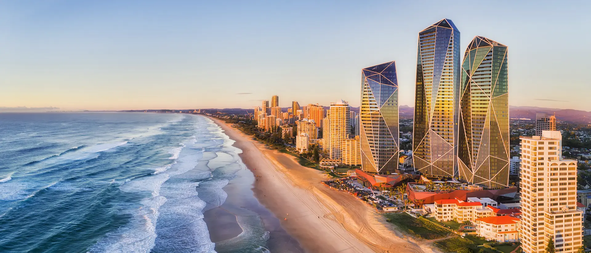 Rising sun shining on modern urban towers of Surfers Paradise in Australian Gold Coast facing endless waves of Pacific Ocean.