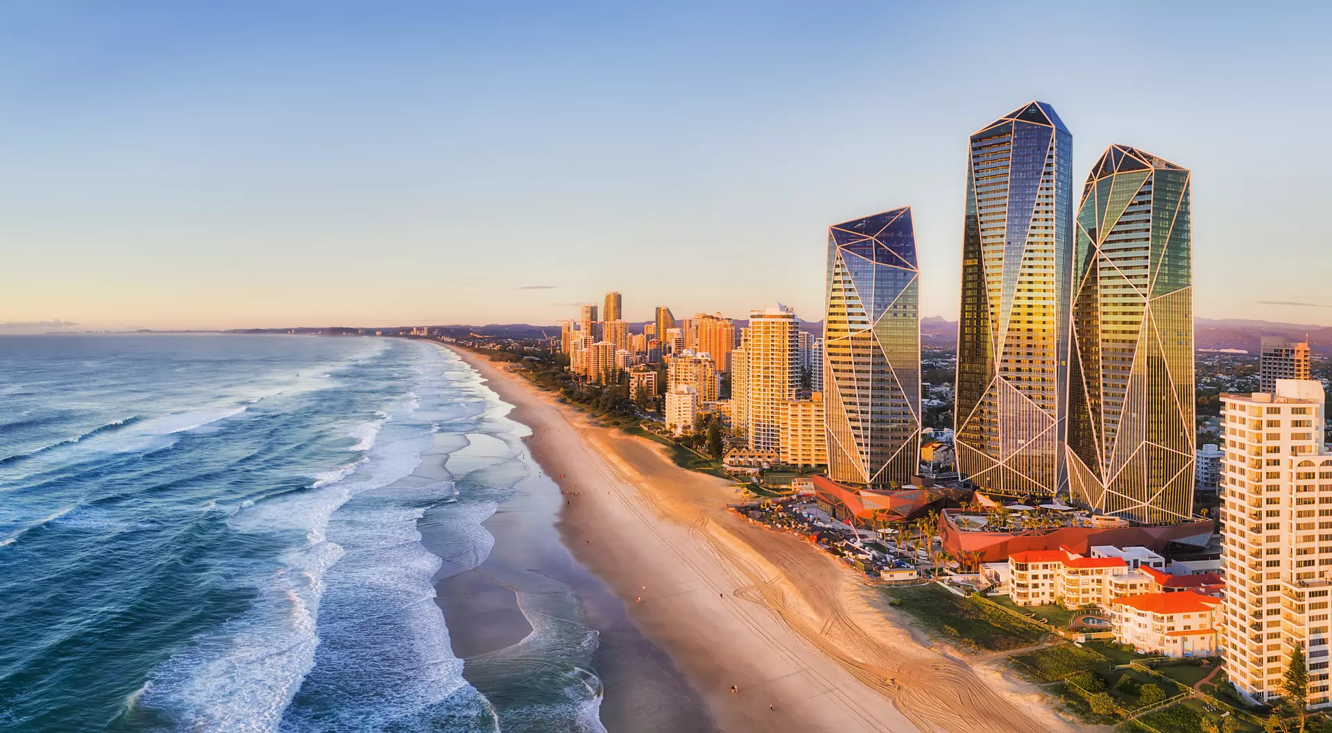 Rising sun shining on modern urban towers of Surfers Paradise in Australian Gold Coast facing endless waves of Pacific Ocean.