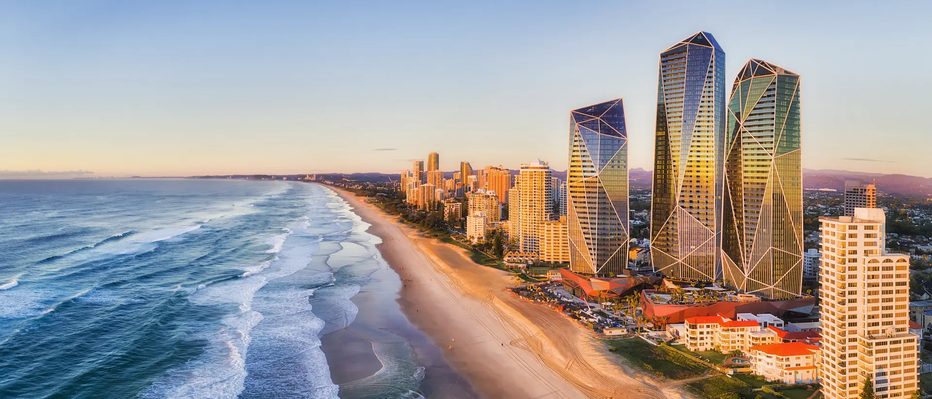 Rising sun shining on modern urban towers of Surfers Paradise in Australian Gold Coast facing endless waves of Pacific Ocean.