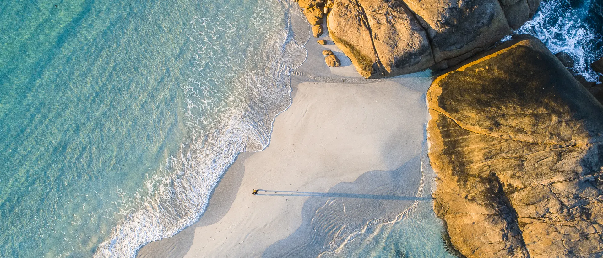 Coastline aerial photograph of aquamarine ocean and man walking along white sandbar beach in Australia