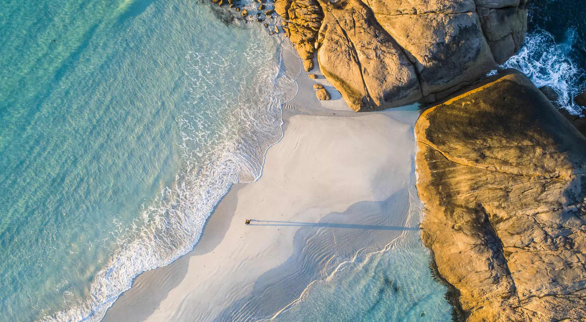 Coastline aerial photograph of aquamarine ocean and man walking along white sandbar beach in Australia