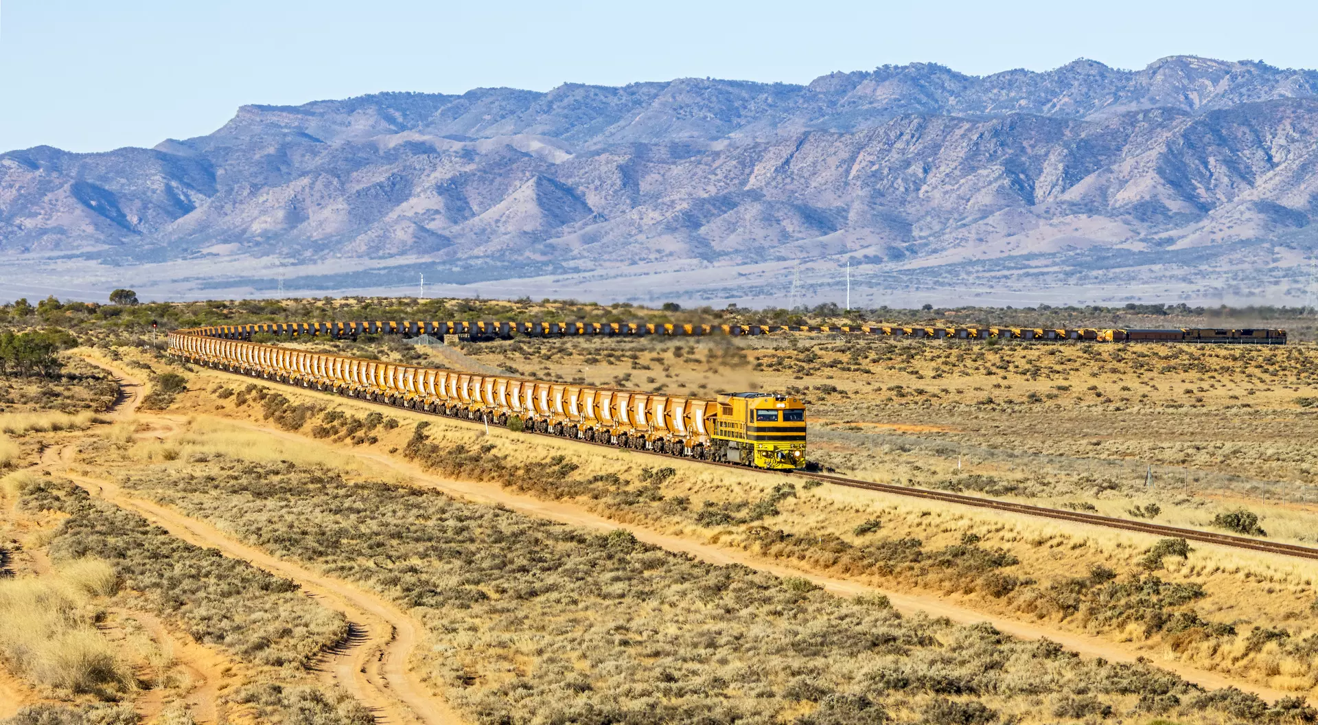View of long, loaded iron ore train from northern South Australian mine with Flinders Ranges background.